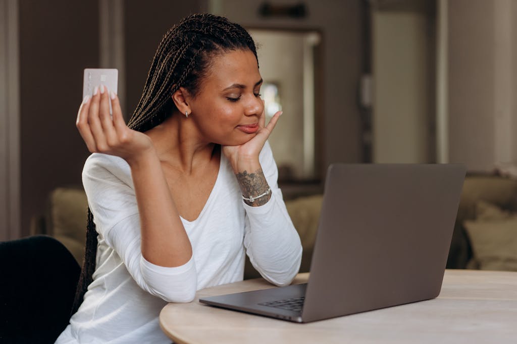 A Woman Sitting at Table with Laptop Holding a Credit. tarjeta de credito asegurada